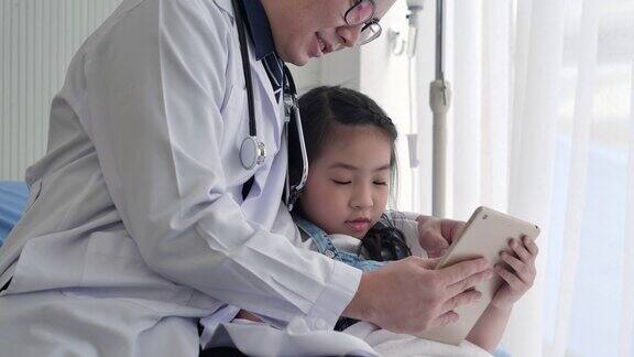 迷人的6岁亚洲小女孩与亚洲儿科医生男性在视频会议上与她的母亲或亲戚视频通话在社交距离期间以防止冠状病毒或Covid-19的流行而坐在医院的床上