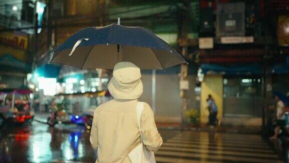 一位年长的妇女在一个雨夜走在夜市上