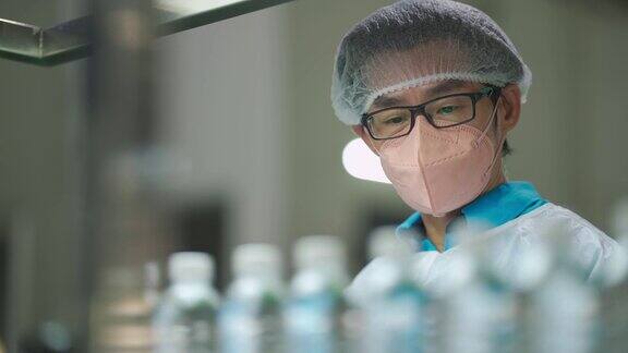 亚洲华人男性生产线工人携带个人防护装备检查瓶装水厂的水瓶