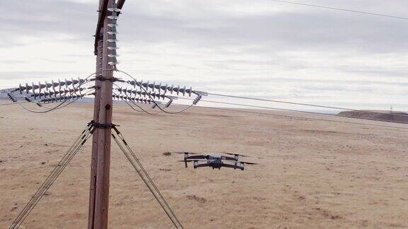 在多云的天空下一架四旋翼无人机在一片棕色草地上检查电力线