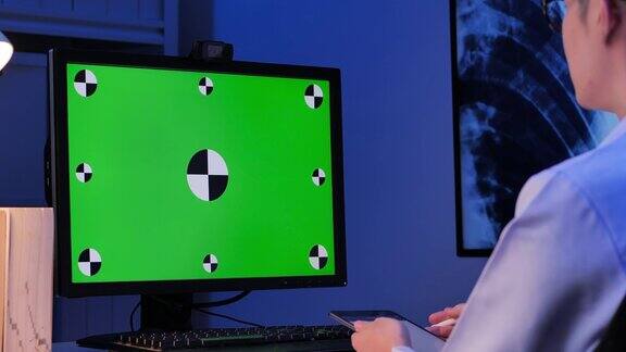 亚洲男医生看绿色屏幕视频会议在远程地点通过电脑在家里晚上工作到很晚居家绿屏