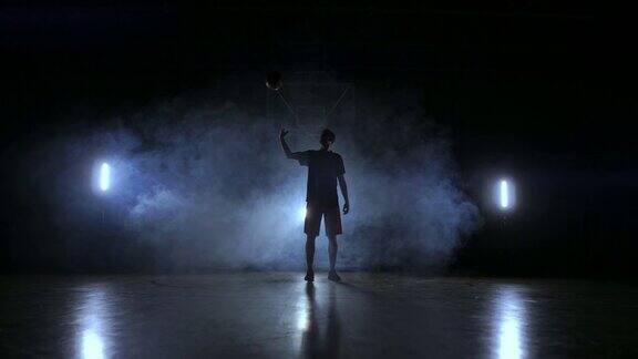 一个篮球运动员的剪影在黑暗的背景与烟雾在篮球场上扔一个篮球看着慢镜头