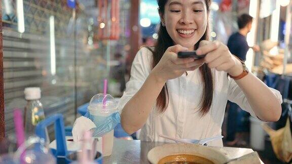 旅游和吃亚洲女性用智能手机捕捉分享探索美食美味的街头小吃在泰国曼谷yaowarat