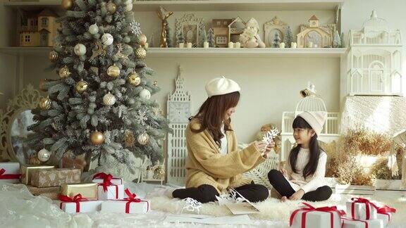 微笑的母亲和女儿在圣诞树旁制作纸雪花
