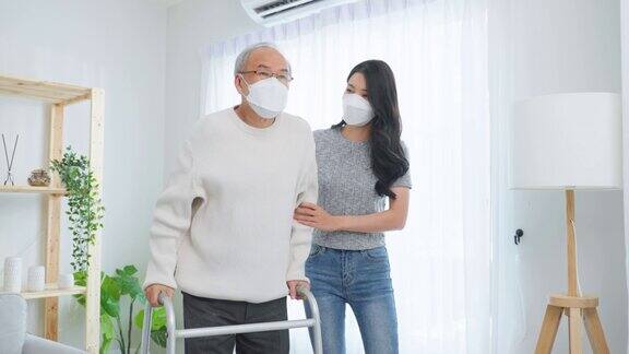 亚洲年轻的女儿支持年长的老人在家里用助行器行走美丽的女孩戴着口罩照顾老人成熟的爷爷病人在客厅里做理疗