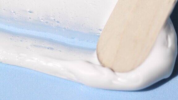 蓝色背景下的白色美容霜样品用木制刮刀进行水疗微距拍摄