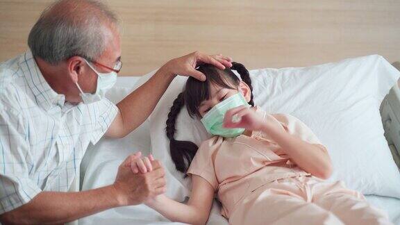 亚洲小女孩戴着口罩躺在康复室的床上父亲来到康复室探望并照顾她的女儿