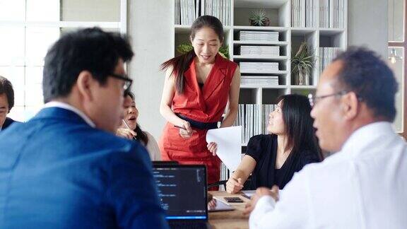 (中景)两个女人在忙碌的办公室聊天时一个同事走近了她们