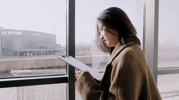 亚洲白领女性站在窗边做笔记