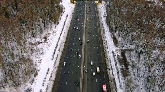 鸟瞰图飞行在高速公路与移动的汽车通过森林在寒冷的冬日