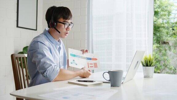 年轻的亚洲商人使用笔记本电脑与同事在视频通话中讨论计划同时在家客厅进行智能工作