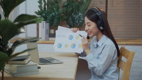 快乐年轻的女性通过耳机在家里使用笔记本电脑工作