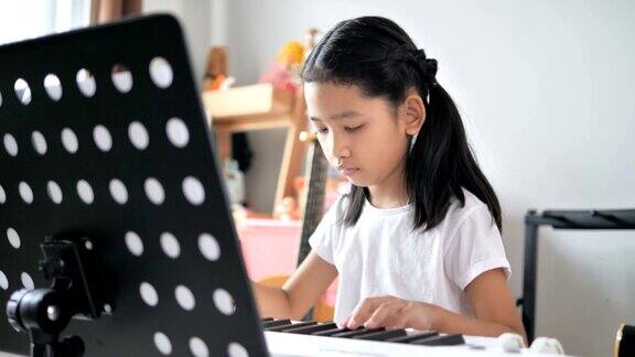亚洲小女孩学习弹奏基本钢琴使用电子合成器键盘初学者音乐器乐自学在家