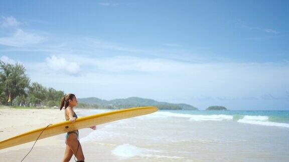 4K肖像亚洲女子泳装拿着冲浪板走在沙滩上在夏天的阳光明媚的日子