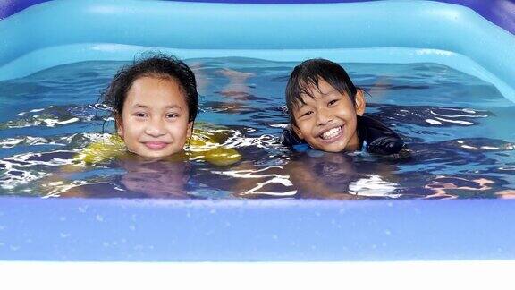 两个亚洲兄弟姐妹一个女孩和一个男孩在炎热的夏日里在游泳池里嬉戏时看着镜头
