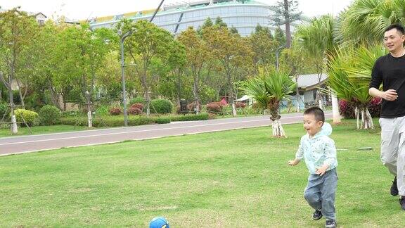 这个孩子正在草地上和他的爸爸和奶奶玩球