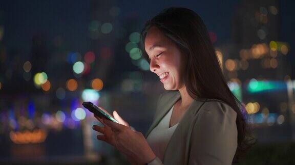 亚洲女人晚上在城市里用美丽的散景用手机
