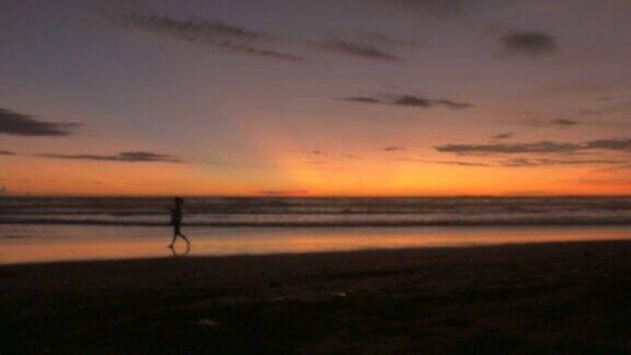 日出或日落时一个人沿着沙滩上的沙滩行走的剪影