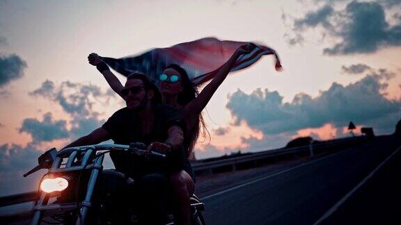 一对年轻的摩托车夫妇骑着摩托车挥舞着美国国旗