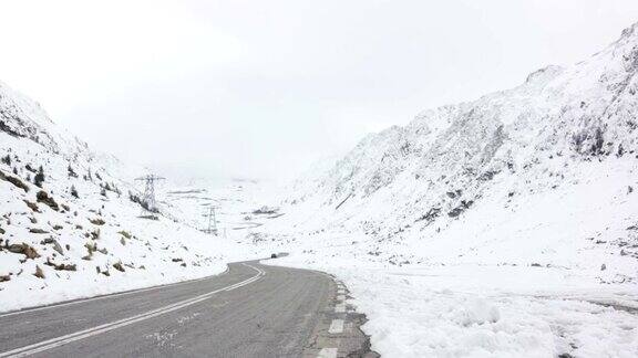 一辆黑色轿车在雪山之间的发夹弯道上行驶