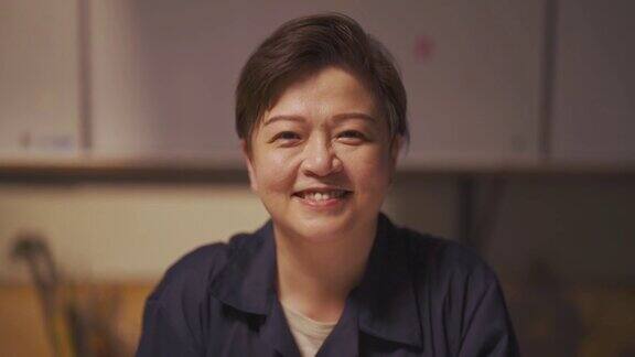 自豪的亚裔中国蓝领女工看着相机在她的车间工作台上微笑
