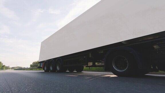 在高速公路上行驶的带有拖车的货运卡车白色卡车运送货物在清晨的几个小时-非常低的角度驾驶通过近距离拍摄