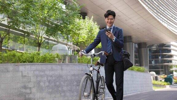 年轻的商人推着他的自行车看着他的手机