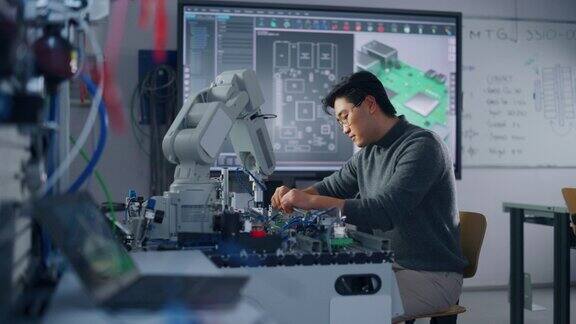 亚洲男性工程师坐在桌子上使用机器人手和工程;转身看着镜头机器人在他的控制下移动教育与机器人概念