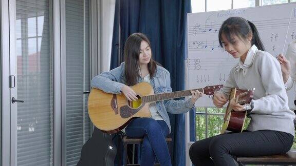 在音乐学校的课堂上一位年轻的亚洲音乐老师正在教授正确的读音和吉他和弦