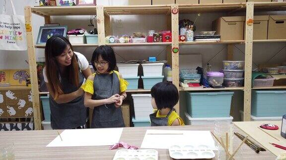 一位亚裔中国美术老师在美术课开始前为她的学生系上围裙