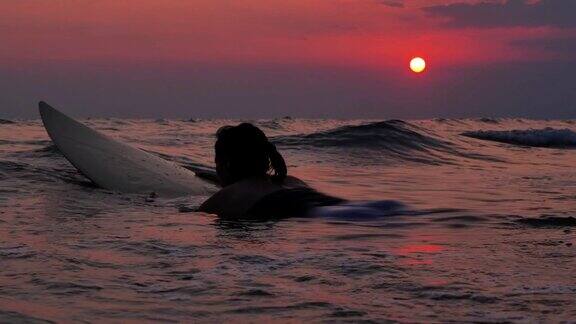剪影快乐美丽性感的冲浪女孩在冲浪板上等待海浪在日落的海滩上运动Cinemagraphs假期-股票