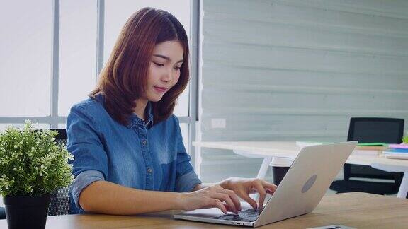 年轻的亚洲商务女性在办公室用笔记本电脑工作