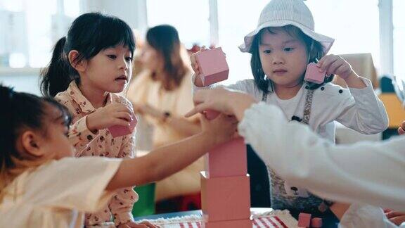 亚洲华人前酷女孩完成最后一块玩具积木建筑塔在蒙特梭利教室