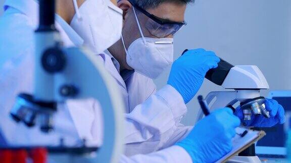 两位亚洲科学家在实验室里通过显微镜进行研究