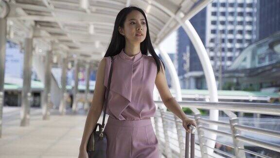 年轻的亚洲女商人在现代化的城市建筑中拖着一个手推车女性出差