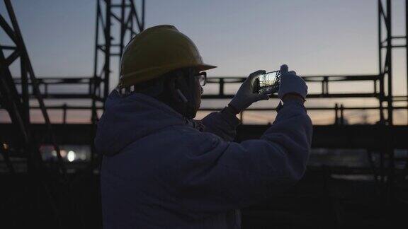 晚上亚洲高级工程师用智能手机检查工业设备的运行情况