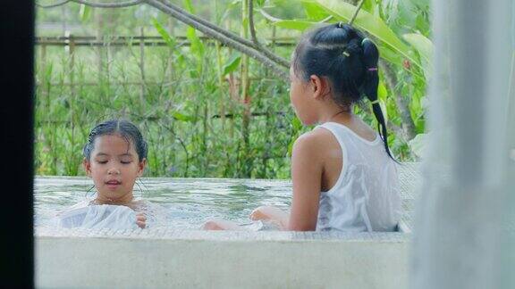 两个亚洲小女孩在外面的游泳池里洗澡和玩耍