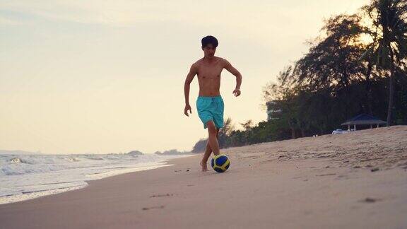 亚洲年轻男子在夏天独自在沙滩上踢足球迷人的男士旅行者感到快乐和放松踢一场足球比赛同时在热带海岛度假旅行
