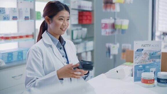 药店收银柜台:专业亚洲女性药剂师销售药品包装讲解如何使用客户使用非接触式支付终端和信用卡支付