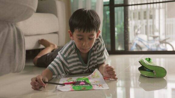 可爱的亚洲男孩有乐趣躺在地板上画画和画画