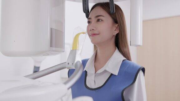 在一台全景x光机上牙医正对着一个女人被咬的伤口在一家牙科诊所一名穿着铅围裙的妇女静静地站在那里一架全景x光机在她头上绕来绕去