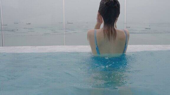 亚洲漂亮的年轻女子在蓝色的泳衣游泳在酒店游泳池看海在暑假