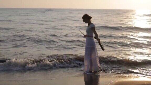 十几岁的女孩走在日落海滩上的小提琴