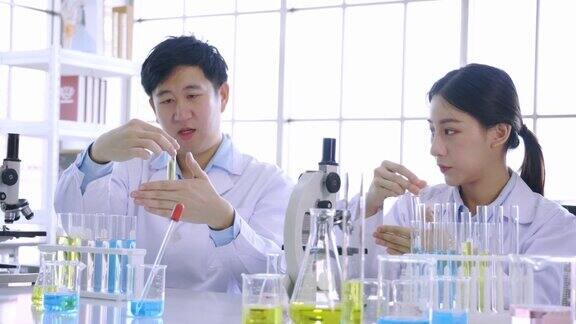年轻的亚洲女性和男性同事科学家在生命科学研究实验室使用显微镜和拿着试管