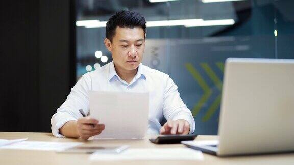 忙碌的员工会计簿记在办公室工作的工作场所计算利润税文书工作日常集中亚洲男性企业家经理分析统计在纸质报告