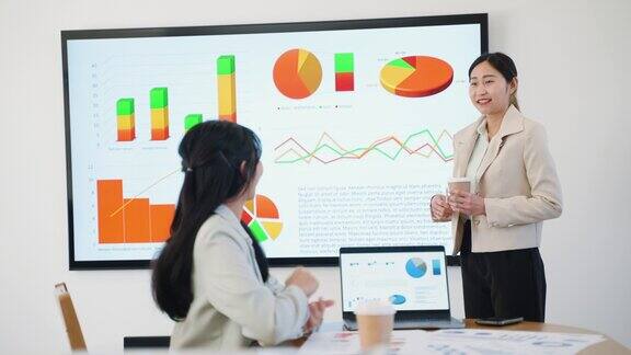 年轻的成年亚洲女性在会议室用大屏幕和她的客户展示商业金融
