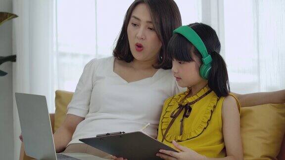 亚洲的小女儿在家里和妈妈一起学习在线课程