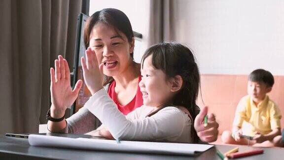 亚洲母亲教女儿用铅笔画画而父亲则在客厅用儿童电视玩电子游戏