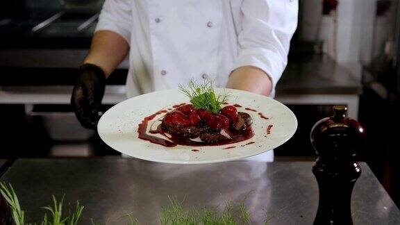 厨师端着一盘牛排和草莓酱在餐厅厨房里