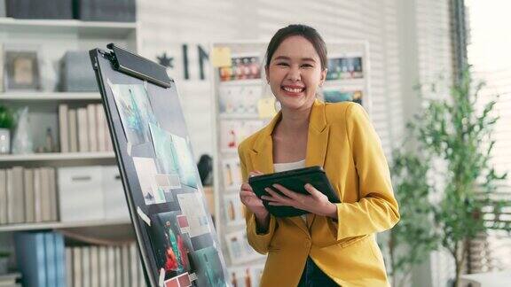 自信的创意机构亚洲女性产品设计师站在微笑肖像拍摄同时在现代工作室车间办公室与纸图表和平面设计板日光